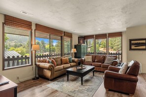 A living room with leather sofas, a coffee table, and large windows with blinds. - Leavenworth Retreat with Pool & Hot Tub (Leavenworth)