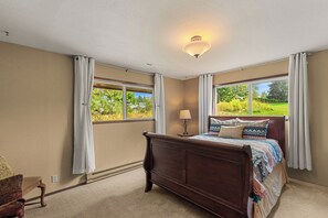A bedroom with a large bed, two windows with curtains, a ceiling light, and a view of greenery outside. - Leavenworth Retreat with Pool & Hot Tub (Leavenworth)