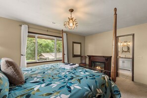 A bedroom with a bed, a fireplace, a window, and a mirror.