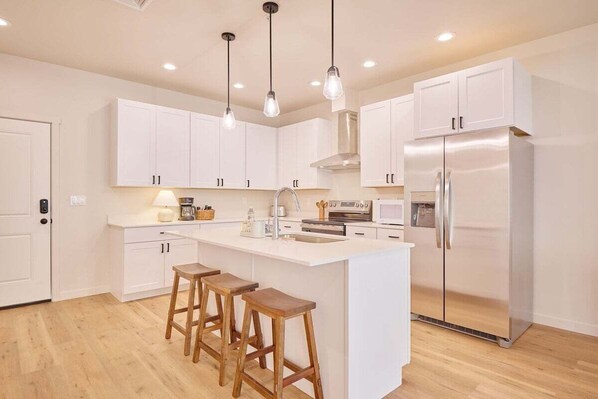 A modern kitchen with white cabinetry, a central island with stools, stainless steel appliances, and pendant lighting. - Riverwalk Suites, #210 Your Riverside Retreat! (Cashmere)