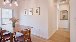 A dining area with a wooden table and chairs, a chandelier, framed pictures on the wall, and a window with a view. - 2BR/2BA Riverfront Condo w/ Deck (Cashmere)