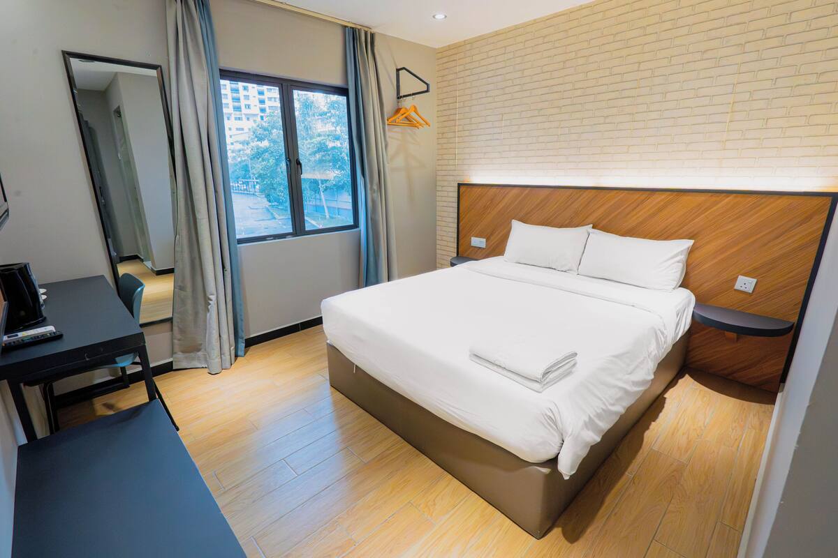 Hotelkamer met een bed, een bureau, een stoel, een raam met gordijnen en een metselwerk muur.