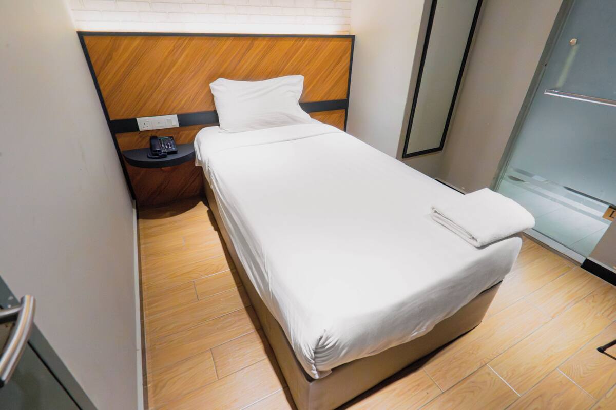 Hotelkamer met een houten hoofdeinde, een enkel bed, een nachtkastje met een telefoon en een glazen deur naar een badkamer.