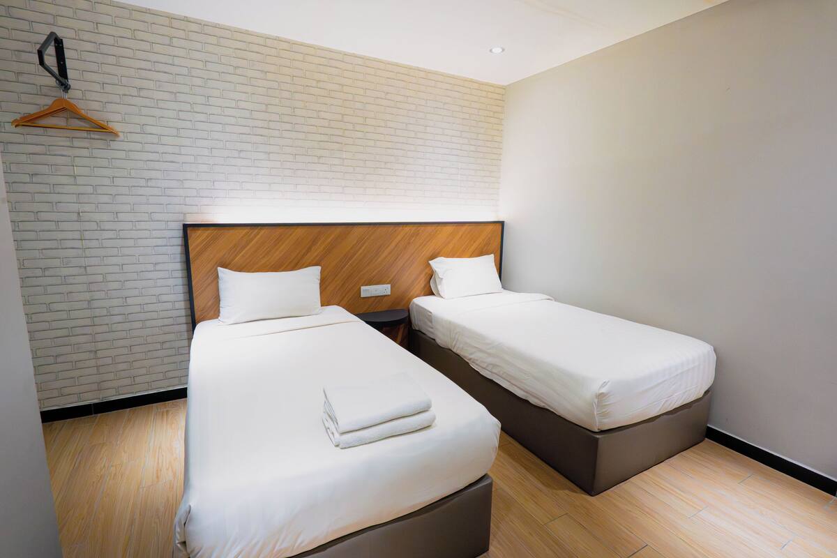 Een hotelkamer met twee bedden, een muur met baksteenmotief en een houten hoofdeinde.