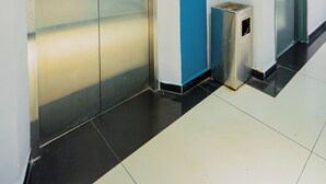 Ein Flur mit blauer Akzentwand, einem Mülleimer und zwei Aufzugtüren.