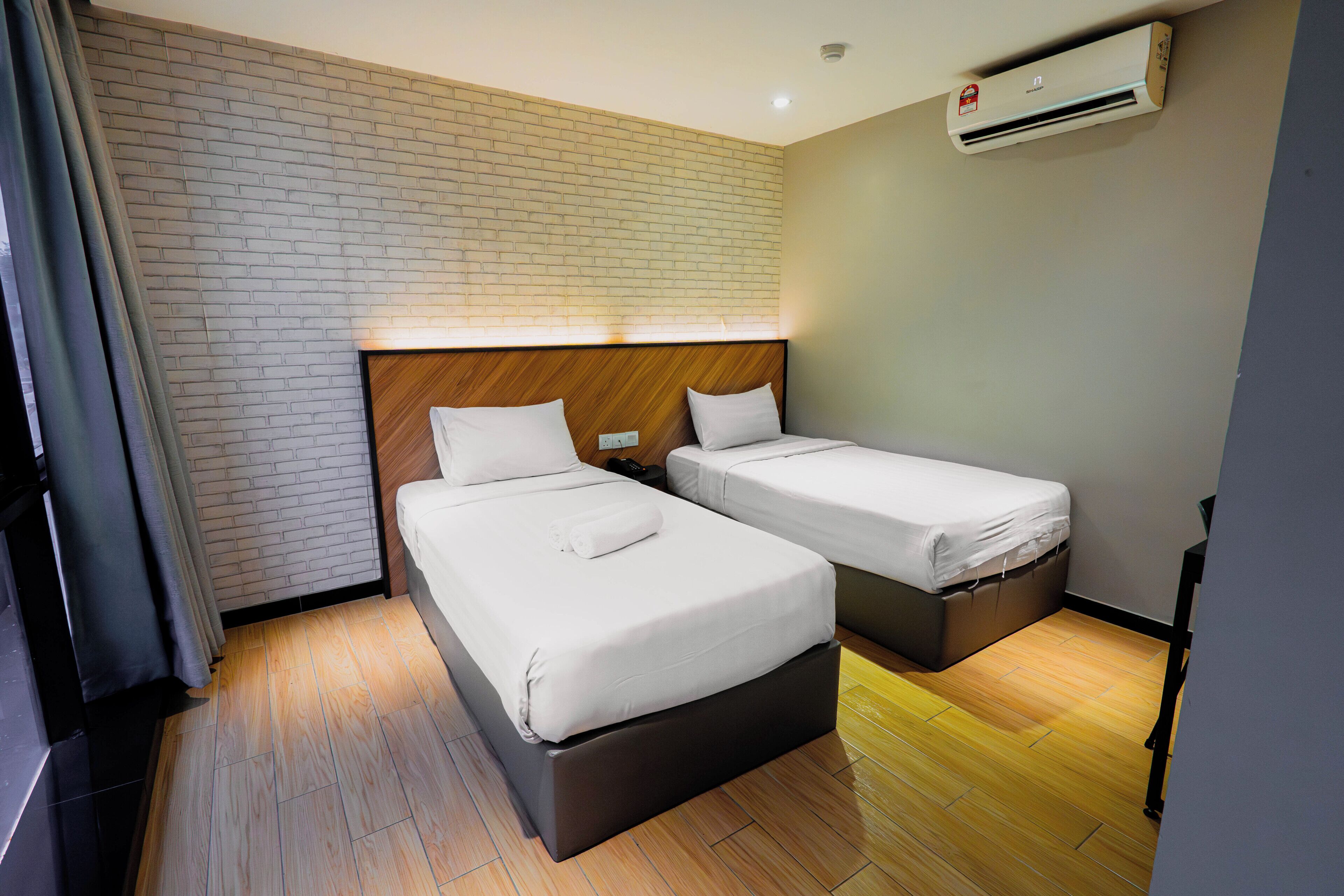 A hotel room with two beds, a brick wall, an air conditioning unit, and a wooden floor.