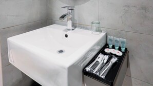 Ein Badezimmer mit einem weißen Waschbecken, einem runden Spiegel, einem Fön und Pflegeprodukten.
