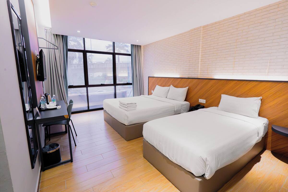 Ein Hotelzimmer mit zwei Betten, einem Schreibtisch, einem Stuhl und einem großen Fenster.