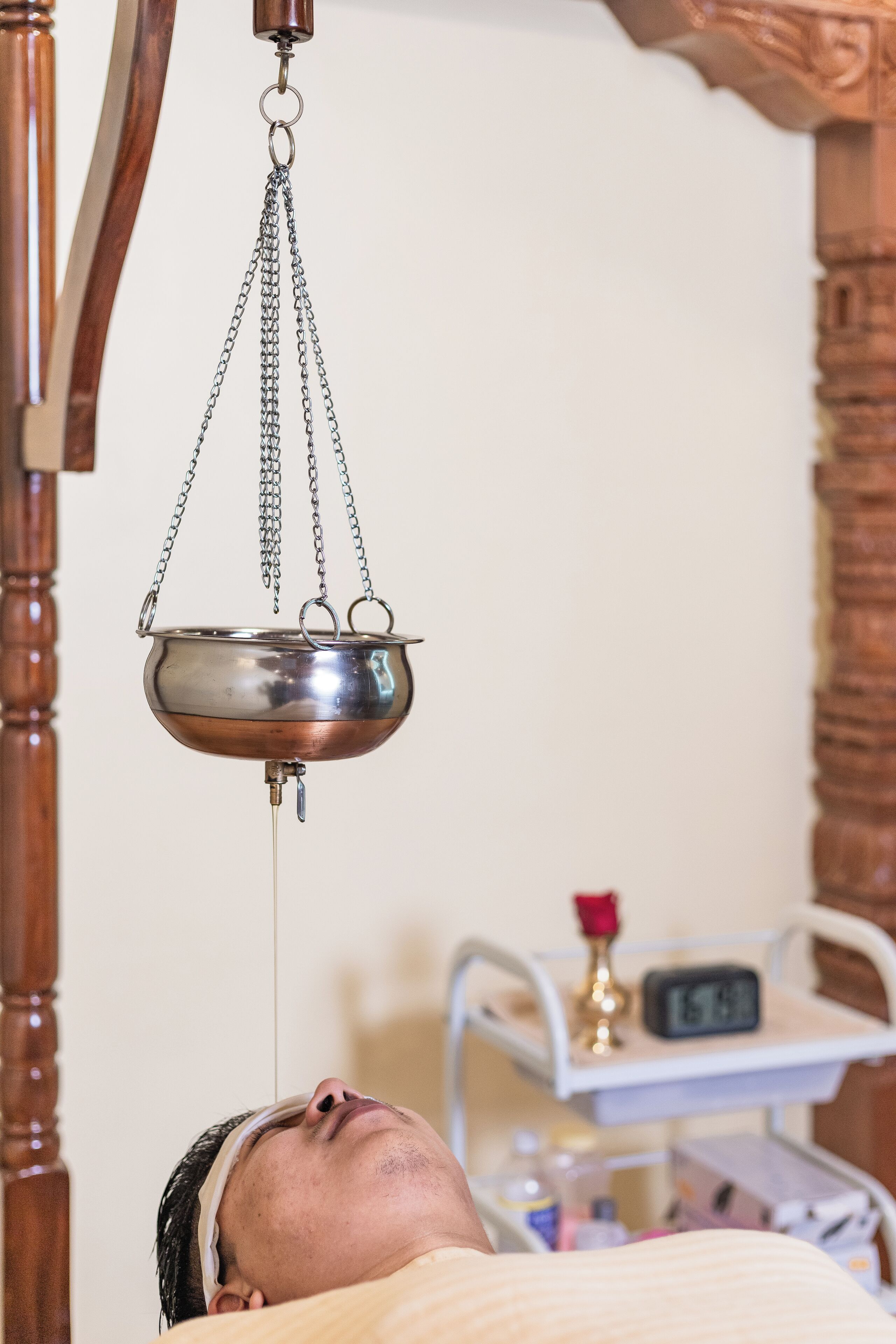 A person lying down with a metal bowl suspended above them, connected to a chain.