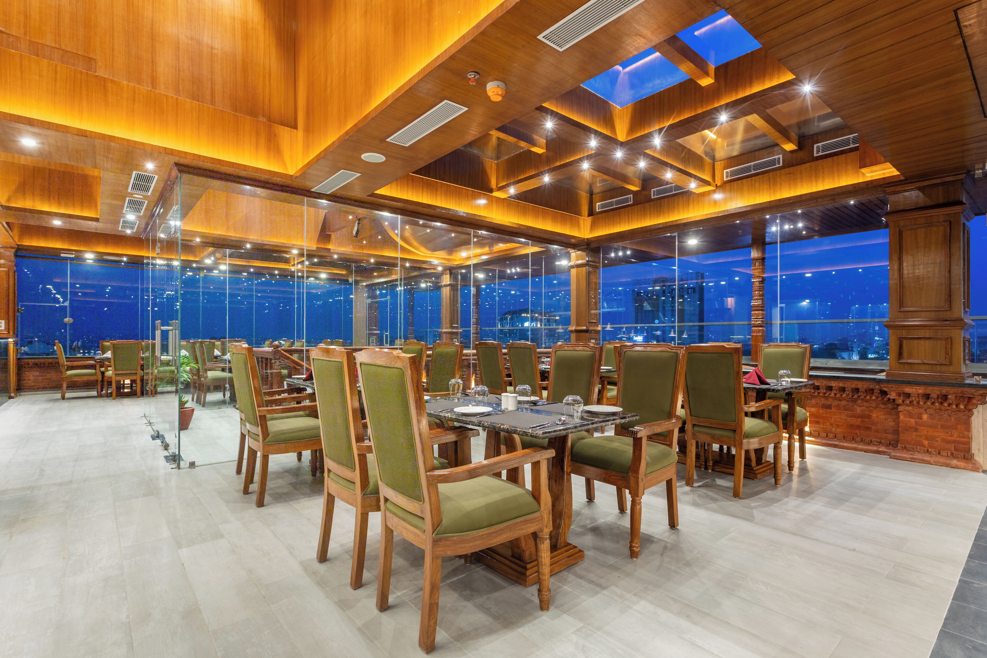 A spacious indoor dining area with wooden furniture and large windows offering city views.