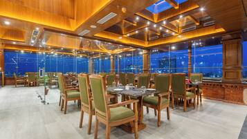 Un amplio comedor interior con mobiliario de madera y grandes ventanales que ofrecen vistas a la ciudad.