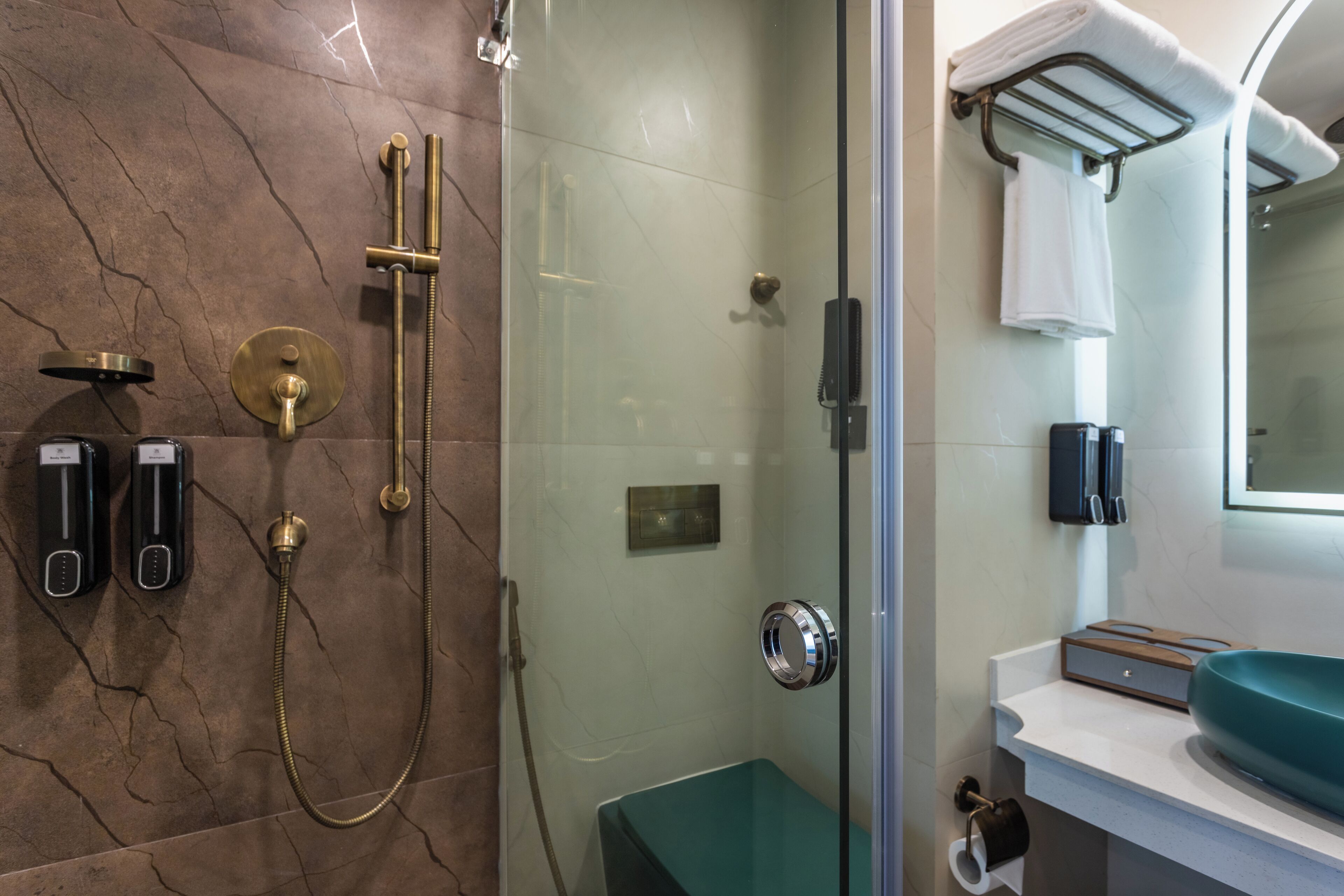 Un bagno moderno con doccia vetrata, parete in marmo, lavabo con lavatoio color petrolio e porta asciugamani.