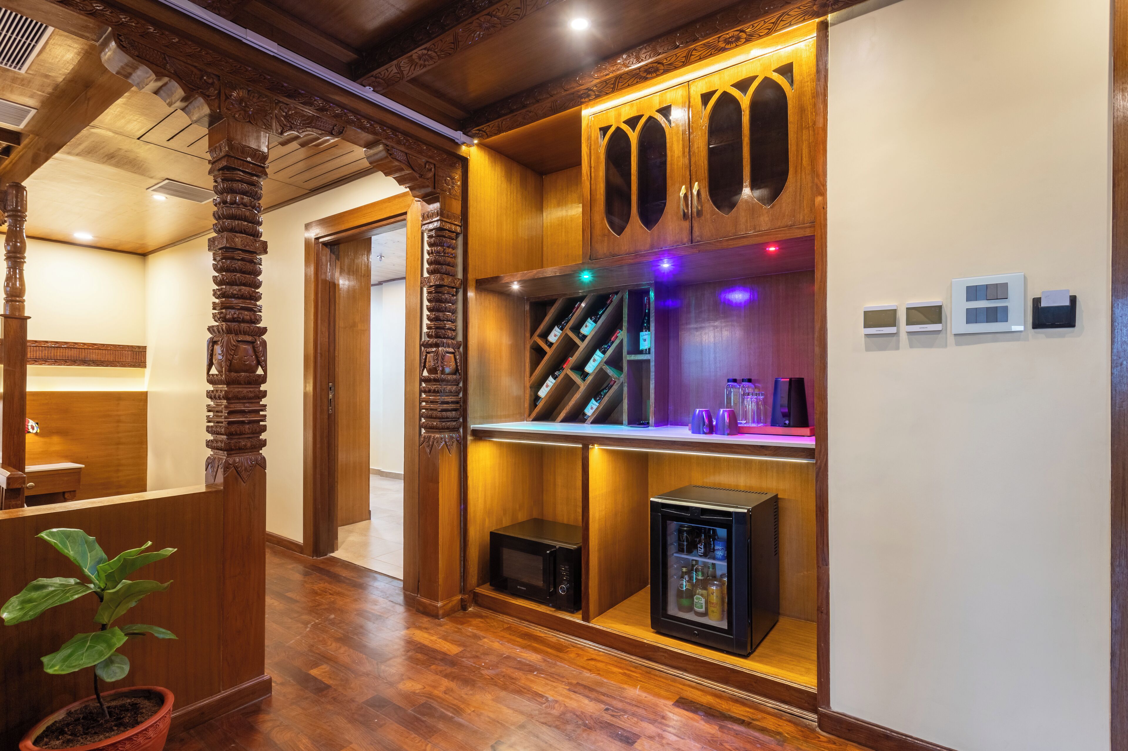 A reception area with wooden decor, a reception desk, a potted plant, a refrigerator, and a wine cooler.