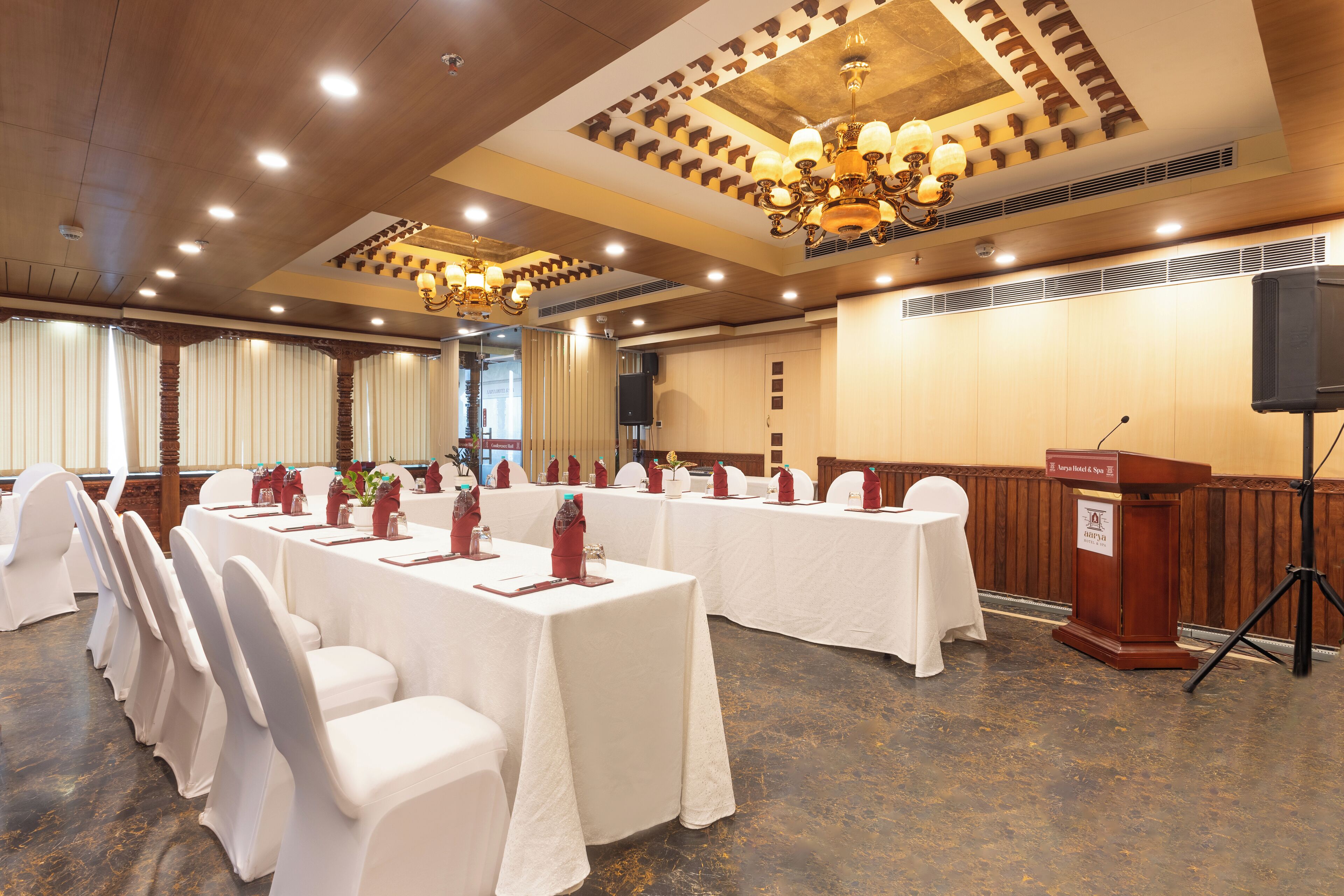 A conference room with white tables and chairs, a podium, and a chandelier.