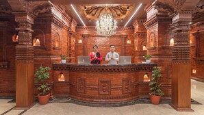 A reception desk with intricate brickwork and a chandelier. There are two individuals behind the desk, each with a laptop. The room has ornate columns and potted plants. - Aarya Hotel and Spa - Eternal Heritage (Kathmandu)