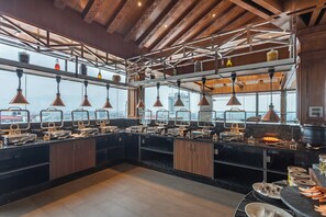 A modern kitchen with multiple serving stations, copper pendant lights, and a view of the city through large windows. - Aarya Hotel and Spa - Eternal Heritage (Kathmandu)