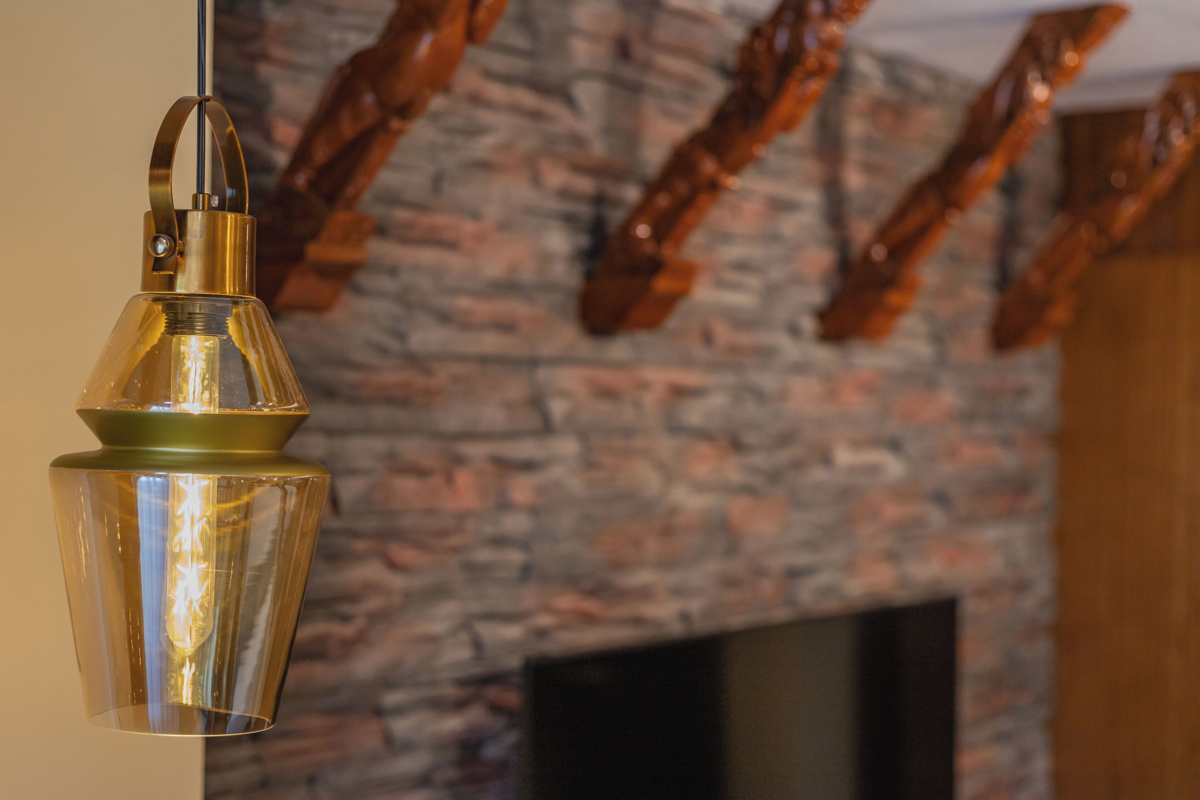 A hanging light fixture with a clear glass shade and a metallic base, a stone wall with a fireplace, and a television mounted on the wall.
