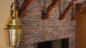 A hanging light fixture with a clear glass shade and a metallic base, a stone wall with a fireplace, and a television mounted on the wall.
