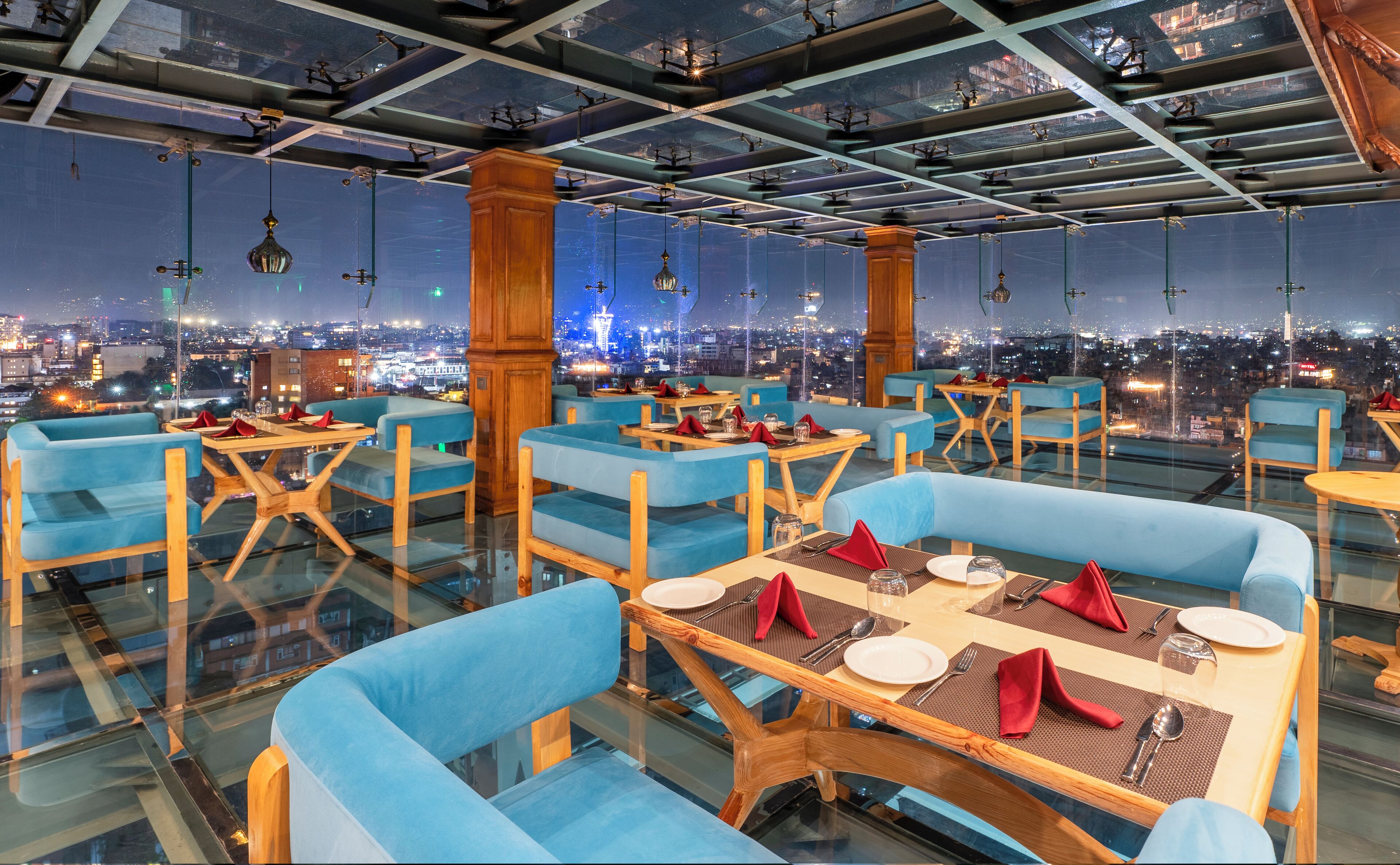 Un restaurant situé dans un immeuble de grande hauteur, avec des sièges rembourrés en tissu bleu, des tables en bois et une vue sur la ville.