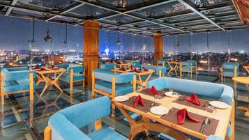 Un restaurant situé dans un immeuble de grande hauteur, avec des sièges rembourrés en tissu bleu, des tables en bois et une vue sur la ville.