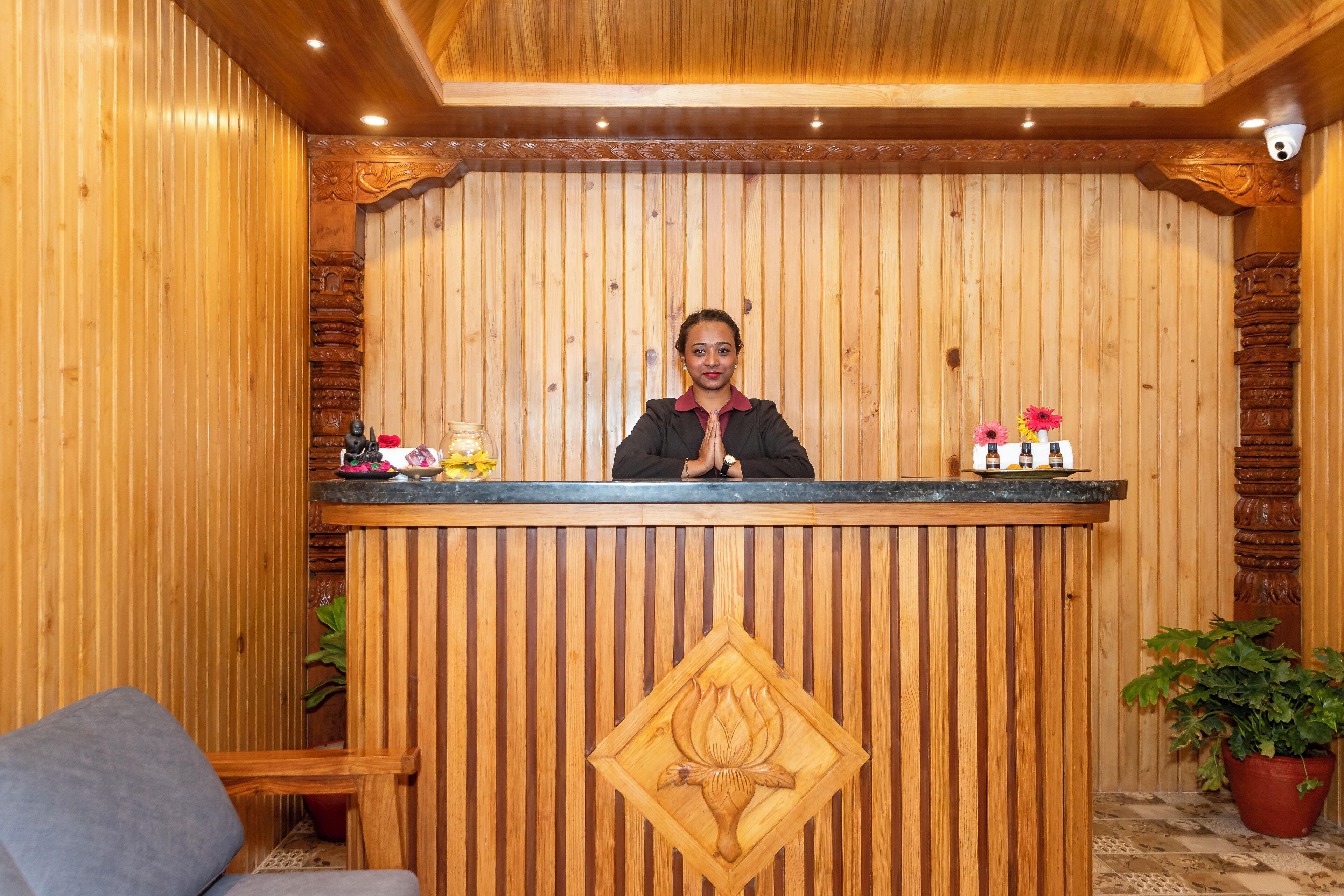 Un mostrador de recepción de madera con un emblema tallado, una planta en maceta y una pequeña mesa con botellas y un florero.