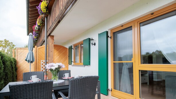 An outdoor patio with a table and chairs, a wooden fence, and a sliding glass door.