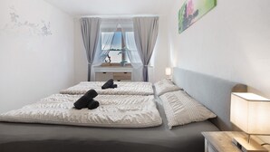 A bedroom with two beds, a nightstand, a lamp, and a window with curtains.