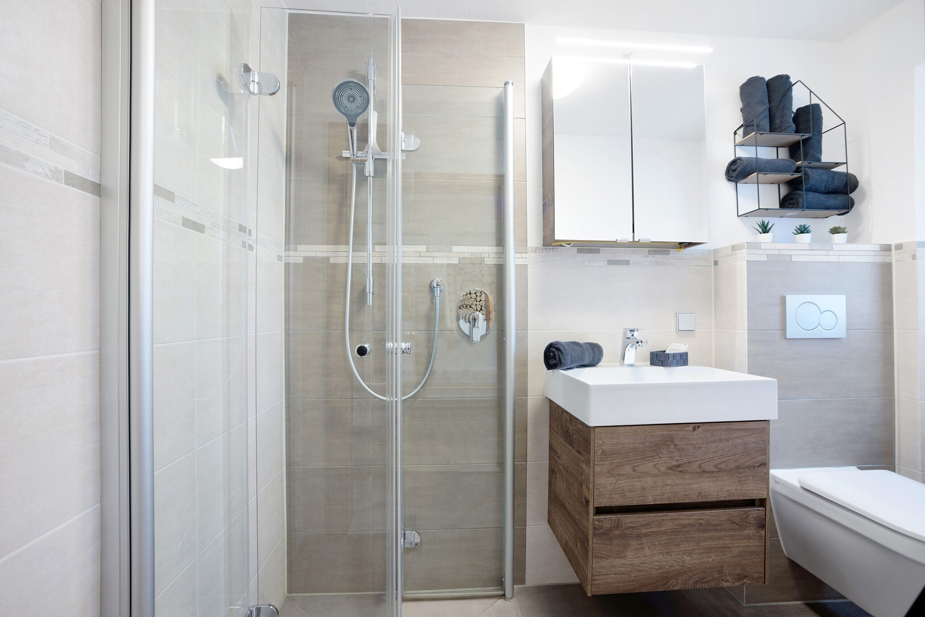 Een moderne badkamer met een douchecabine van glas, een houten wastafelmeubel en een wit toilet.