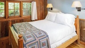 Una habitación de madera con una cama, dos lámparas de pared y un ventanal con cortinas.