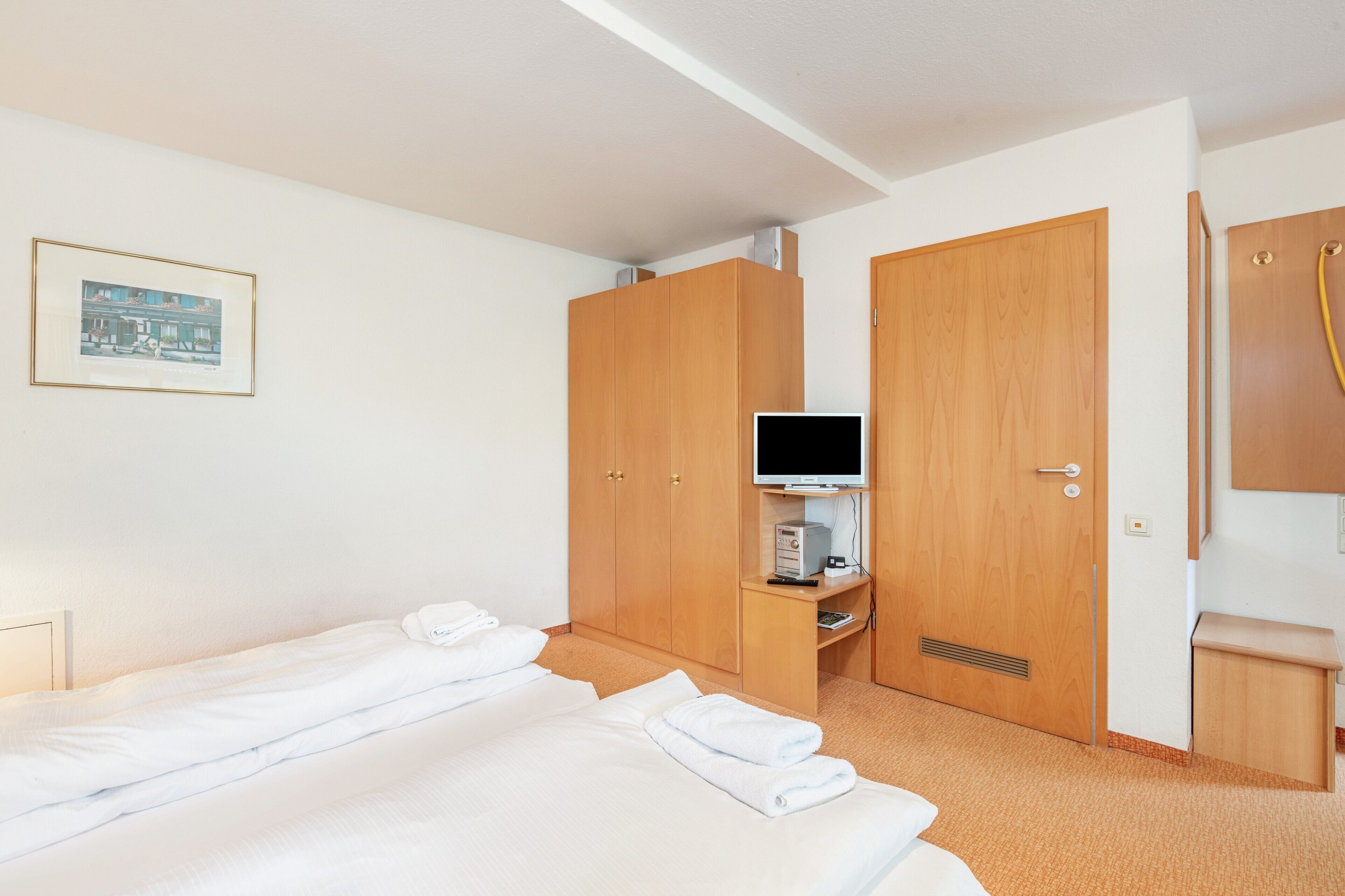 Hotellihuone, jossa on sänky, televisio, puinen vaatekaappi, pieni työpöytä ja seinällä kehystetty taulu.