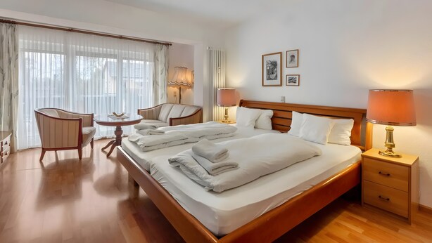 A hotel room with a large bed, bedside tables, a chair, a small table, and a window with curtains. - Room 'Doppelzimmer 3 - Behindertengerecht' with Shared Terrace and Wi-Fi (Bad Bellingen)