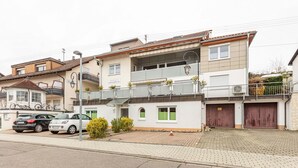 A two-story building with a balcony, a garage, and a parking area with two cars. - Room 'Doppelzimmer 3 - Behindertengerecht' with Shared Terrace and Wi-Fi (Bad Bellingen)