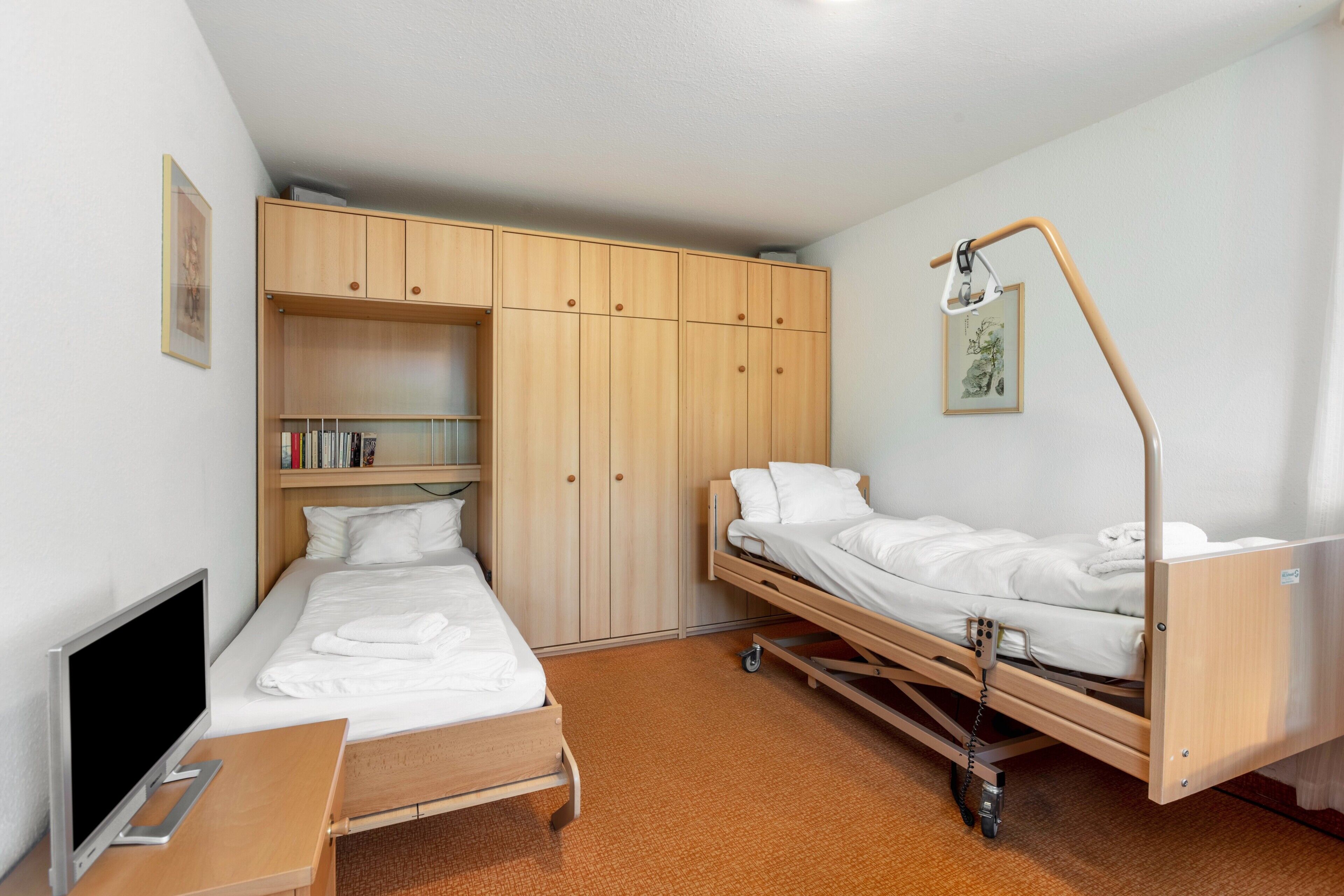 A single-bed room with a desk, a TV, a wardrobe, and a bedside table.