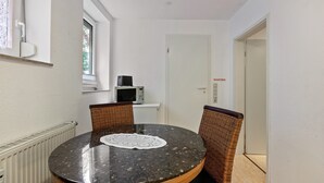 A round table with a lace doily, wicker chairs, a white radiator, a window, and a door with a sign. - Apartment 'Ferienwohnung 7c' with Shared Terrace and Wi-Fi (Bad Bellingen)