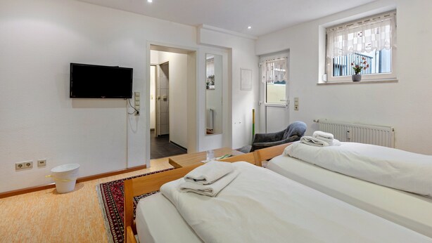 A hotel room with two beds, a television, a window with a view, and a bathroom door. - Apartment 'Ferienwohnung 7c' with Shared Terrace and Wi-Fi (Bad Bellingen)
