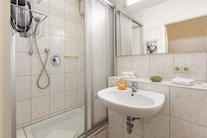 A bathroom with a shower, a sink, a mirror, and a towel rack.