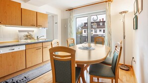 Una cocina moderna con armarios de madera, una mesa de comedor con sillas y vistas a edificios a través de un ventanal.