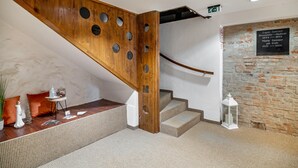 Een houten trap met ronde uitsparingen, een stenen muur met plaquette, en een rieten bankje met decoratieve objecten.