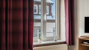 Een raam met gordijnen, een radiator, een kleine plant en een glazen potje op de vensterbank.
