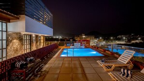 A rooftop pool area with lounge chairs and a view of the city at night. - Redolence Aravali Tree (Udaipur)