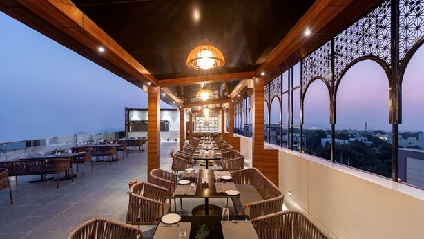 A restaurant with outdoor seating, wooden beams, and large windows offering city views. - Redolence Aravali Tree (Udaipur)
