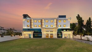 A modern hotel with a symmetrical facade, large windows, and a well-maintained lawn. - Redolence Aravali Tree (Udaipur)