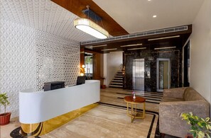 A modern reception area with a white reception desk, a staircase, and a black elevator. - Redolence Aravali Tree (Udaipur)