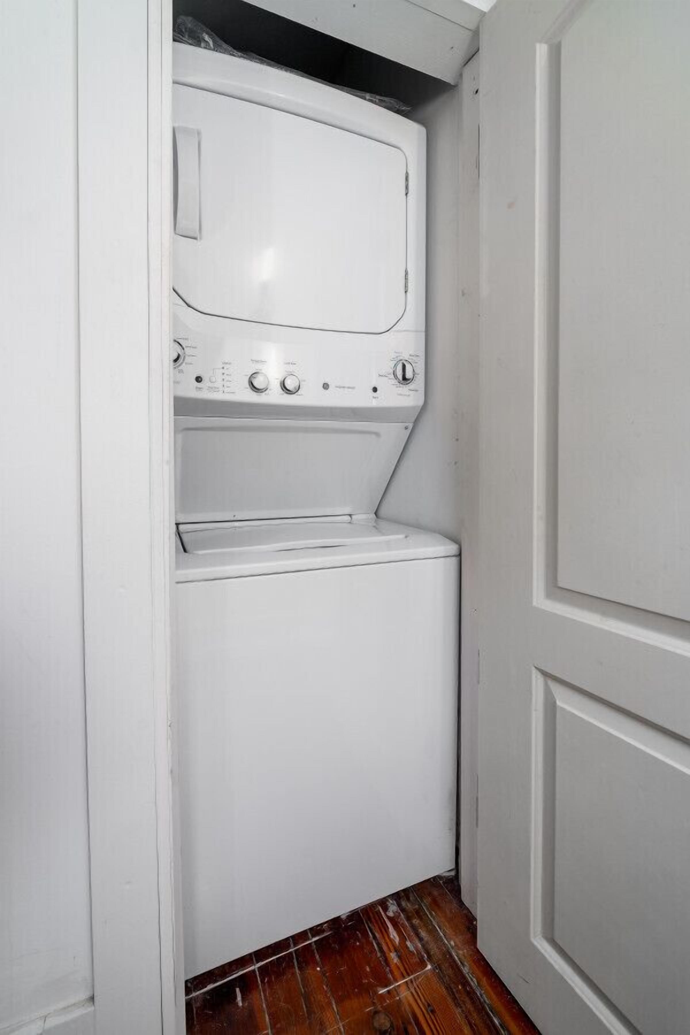A compact laundry room with a front-loading washer and dryer, white walls, and a wooden floor.