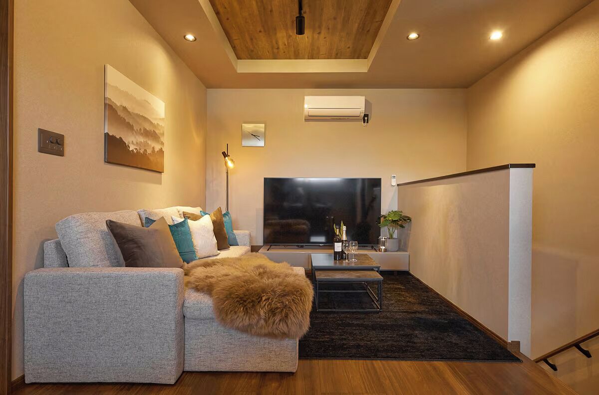 A modern living room with a sofa, a coffee table, a flat-screen TV, and a ceiling light.