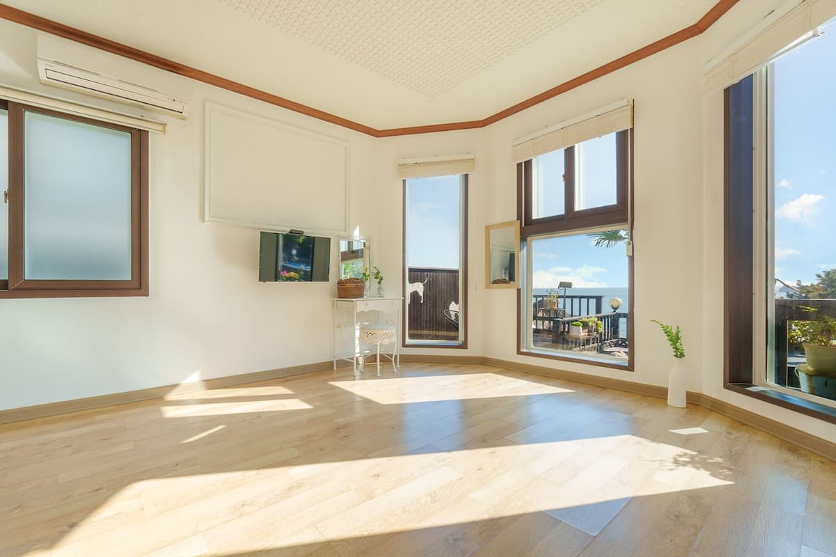 A spacious room with large windows, wooden flooring, and a small white desk with a mirror and decorative items.