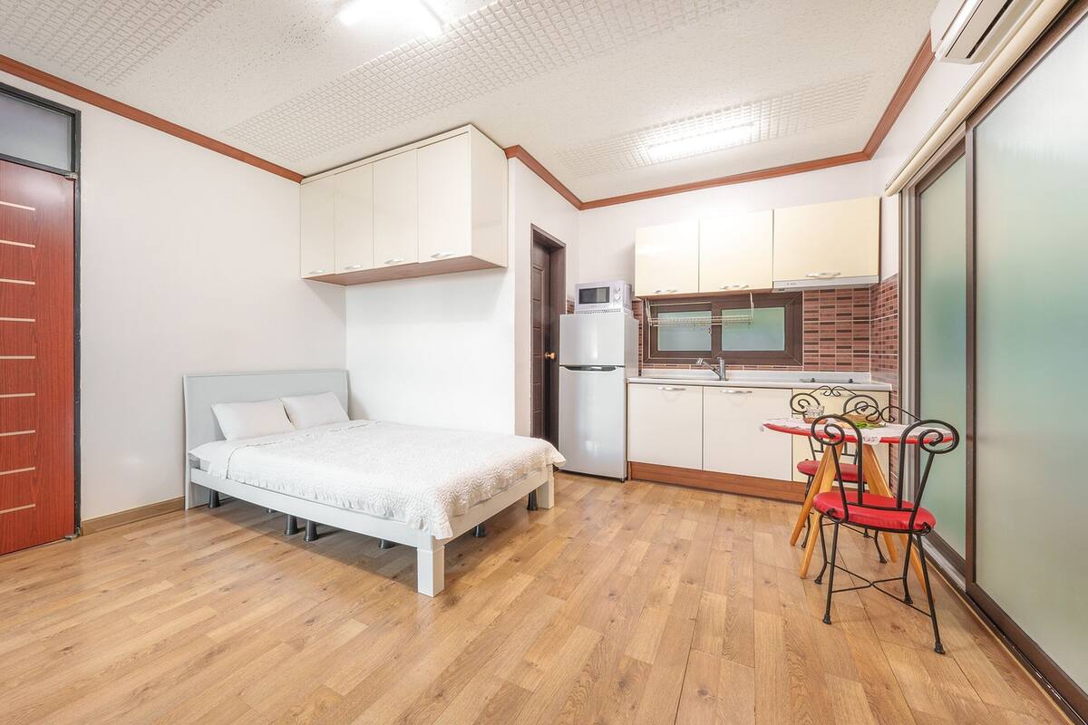 A compact bedroom with a bed, a small kitchenette, and a dining area with a table and chairs.