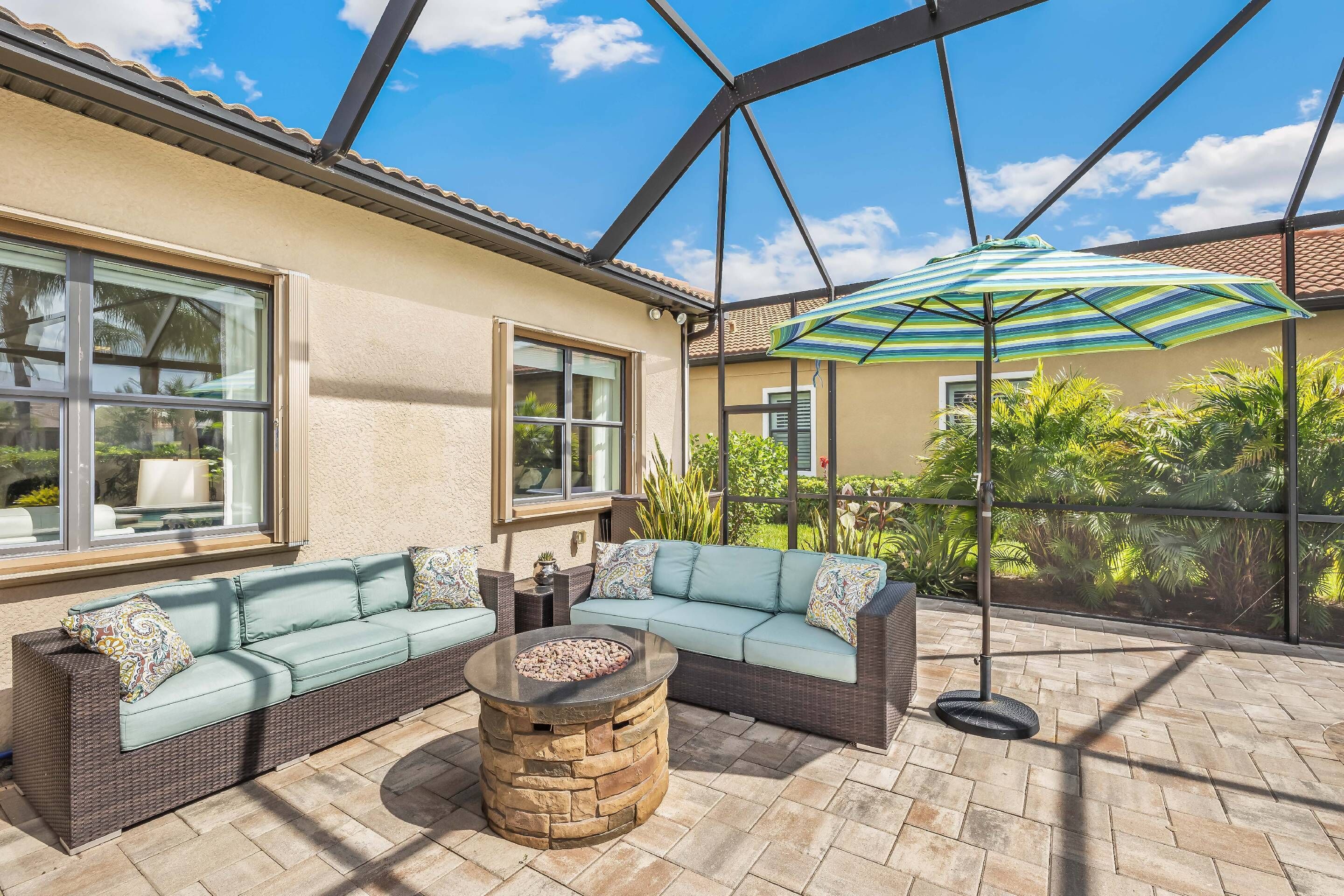 Ein überdachter Patio-Bereich mit einem Steinkamin, einem Ecksofa und einem großen Sonnenschirm.