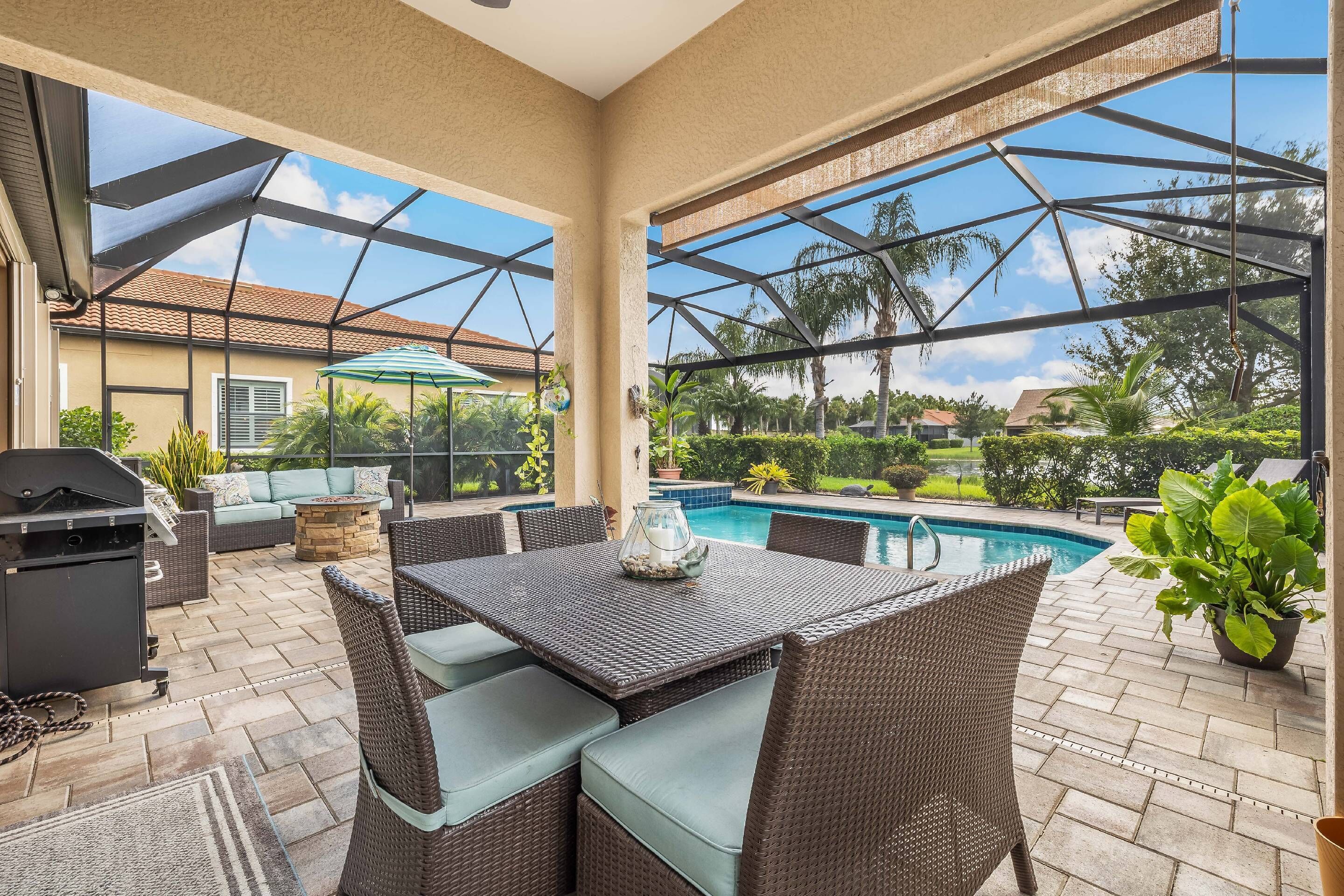 A covered patio with a pool, wicker furniture, and a grill area.