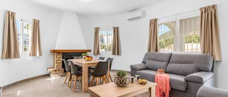 A modern living room with a grey sofa, wooden dining table, and chairs.